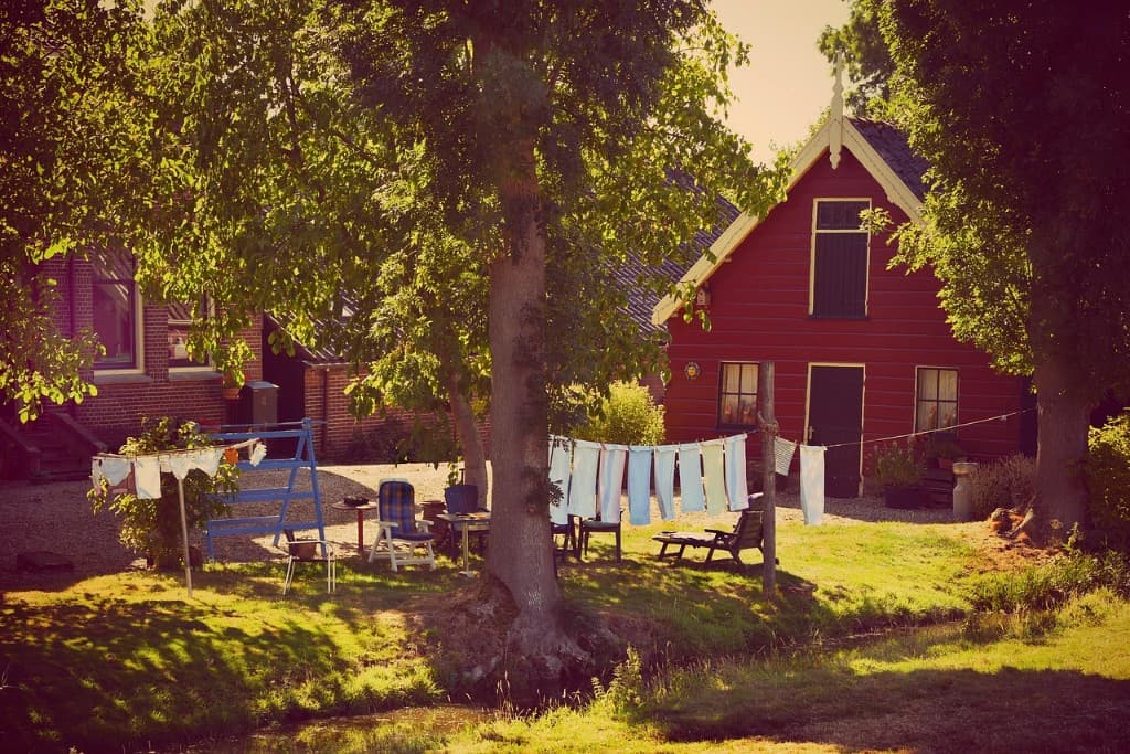 Rotes schwedisches Wirtschaftsgebäude an einem Sommerabend, Wäsche trocknet zwischen Laubbäumen.