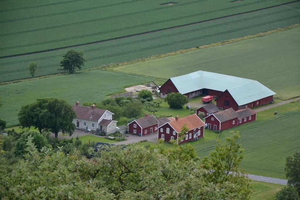 Svensk gård med röda ekonomibyggnader och bostadshus omgiven av gröna fält.