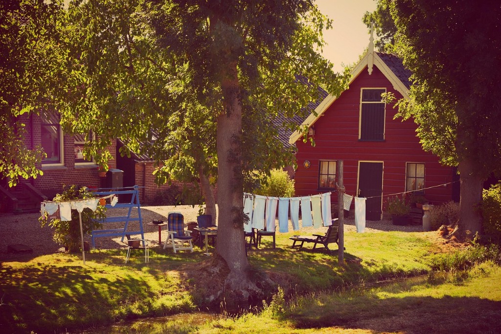 Röd svensk gårdsbyggnad en sommarkväll med tvätt på tork mellan lummiga träd.